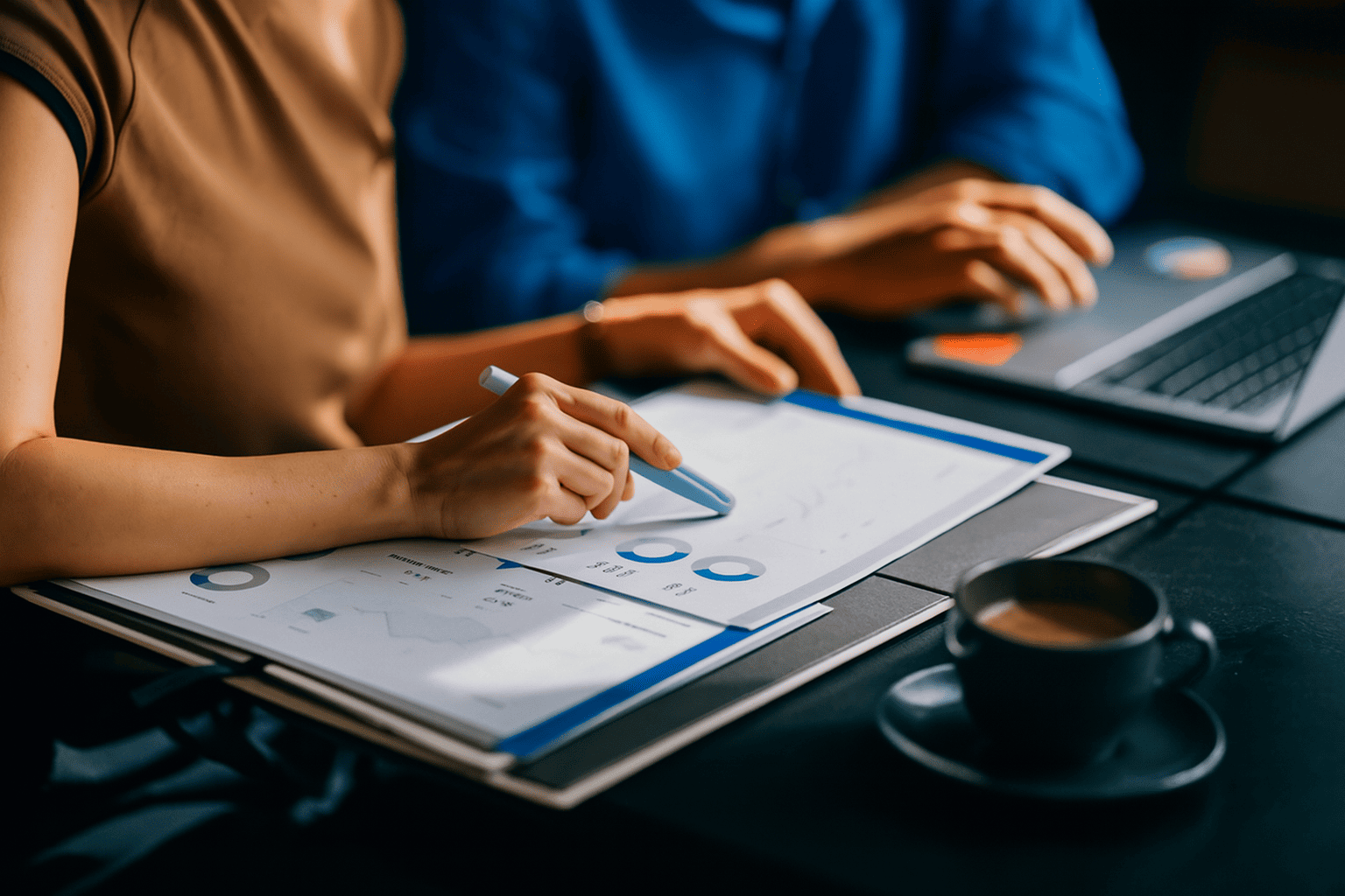 Zwei Personen analysieren Finanzdaten und Investmentstrategien anhand von Unterlagen und Laptop