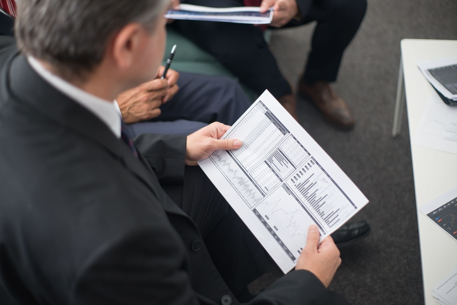 Mann im Anzug prüft im Sitzungssaal einen Finanzbericht mit Diagrammen und Tabellen als Sinnbild für die Due-Diligence von Investoren