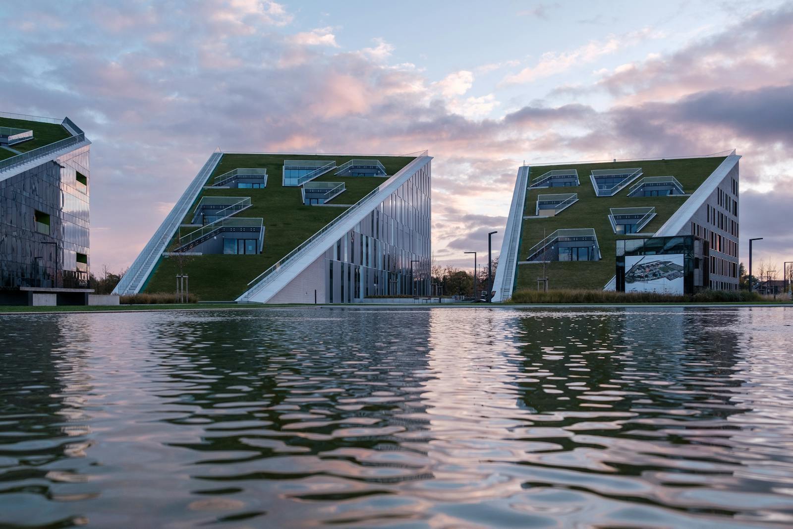 Moderne Gebäude mit begrünten Dächern spiegeln sich bei Sonnenuntergang im Wasser als Sinnbild für nachhaltige städtische Infrastruktur